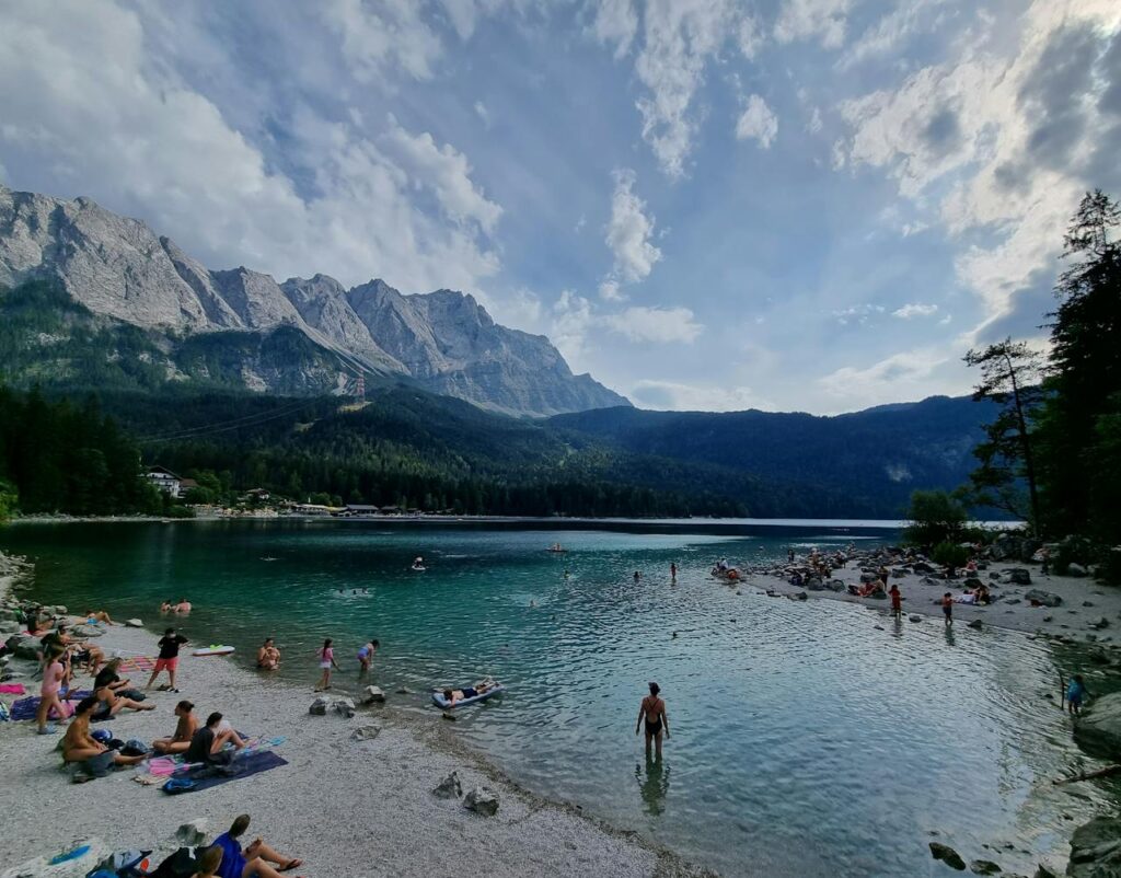 Serene scene of Lake Eibsee with mountains, clear water, and people relaxing by the shore.
